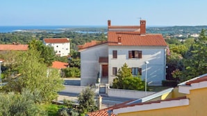 A two-story building with a red-tiled roof, surrounded by greenery and other buildings, overlooking a coastal landscape. - Apartment B&B by Interhome (Medulin/Ližnjan)