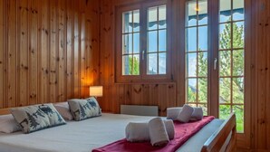 A wooden-paneled room with a large bed, two windows, and a view of greenery outside. - Vacation home Bivak by Interhome (Nendaz)