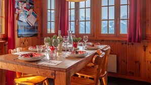 A wooden dining room with a table set for two, a hanging lamp, and a view of mountains through large windows. - Vacation home Bivak by Interhome (Nendaz)