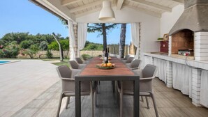 Un espace extérieur aménagé pour les repas, avec une longue table et des chaises en bois, une cheminée en pierre et une vue sur le paysage environnant.