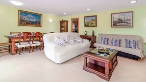 Una sala de estar con un sofá blanco, una mesa de centro de vidrio y un comedor con sillas de madera y una mesa.
