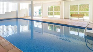 Une piscine intérieure à l’eau d’un bleu limpide, avec des murs carrelés et de grandes fenêtres.