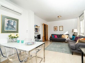 A modern living room with a dining area, a gray sofa with colorful cushions, a white table, and a blue rug.