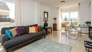 Un salon moderne avec un canapé gris, une table basse et un coin repas comprenant une table et des chaises en verre.