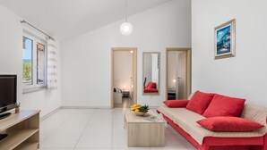 Un salon moderne avec un canapé rouge, une table basse en bois sur laquelle sont disposés des fruits, un téléviseur et un tableau accroché au mur.