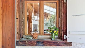 Eine Holztür mit Fensterglas, ein rustikaler Außenbereich und ein kleiner Podeststufenaufgang zu einer weißen Wand.
