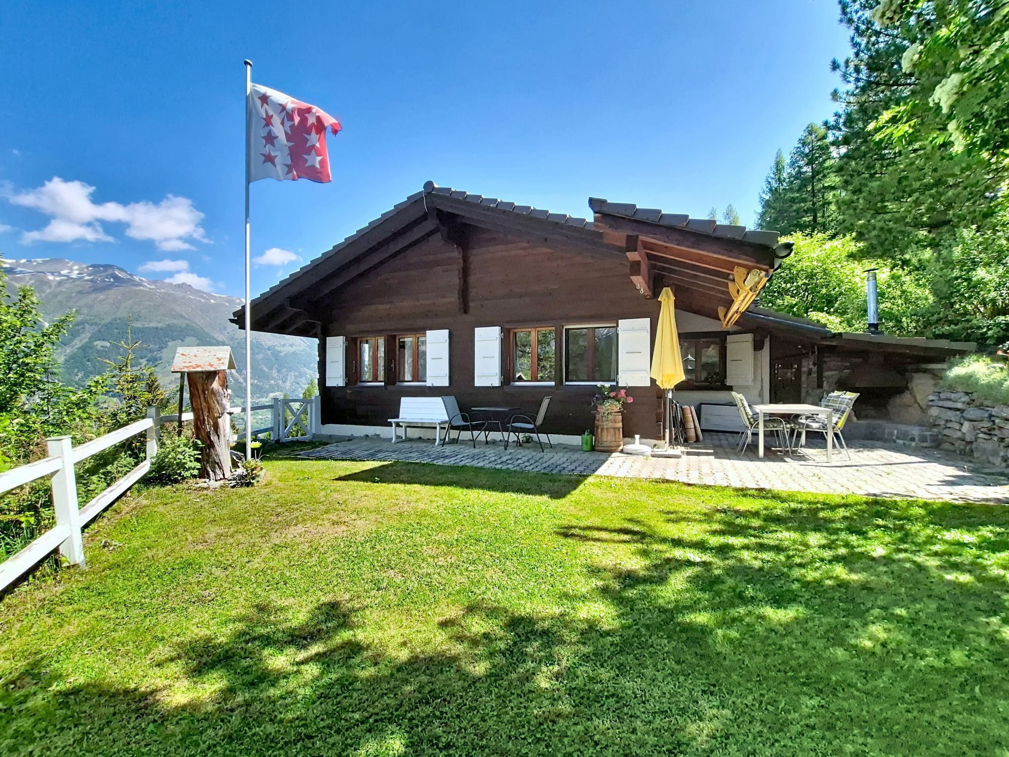 Eine Holzhütte mit Terrasse, Sitzgelegenheiten im Freien und einer Flagge.