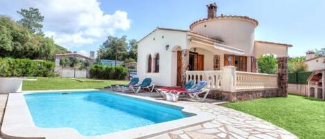 Una villa con piscina, patio de piedra y jardín.