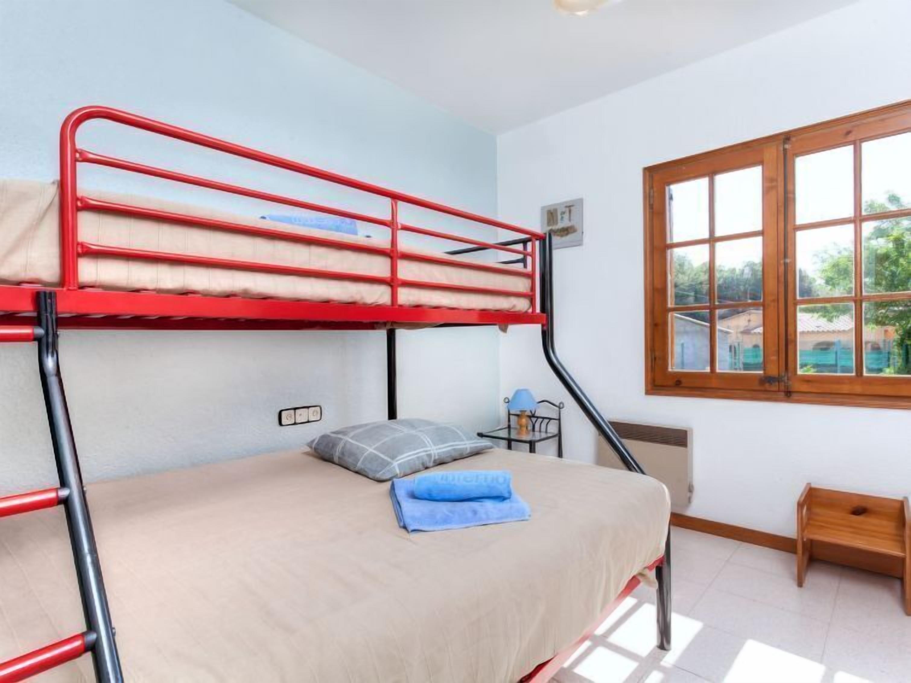 A bunk bed room with a window, a small table, and a lamp.