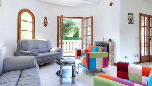 Ein geräumiges Wohnzimmer mit grauem Sofa, bunten Sesseln, einem Glastisch und einem Kamin.