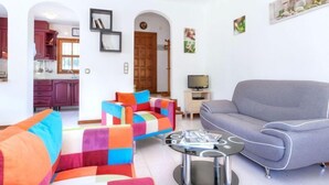 Ein modernes Wohnzimmer mit einem grauen Sofa, bunten Sesseln und einem Glastisch.