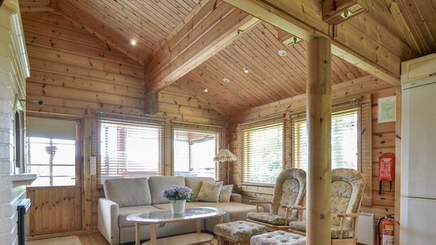 A wooden cabin interior with a sofa, armchairs, a small table, and a fire extinguisher. - Kannelpirtti 1 by Interhome (Liperi)