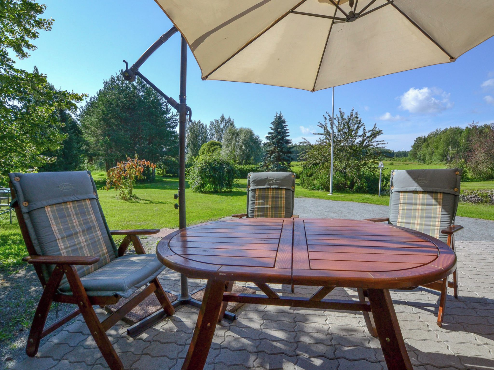 A patio with a wooden table and two chairs, a large umbrella, and a garden view.