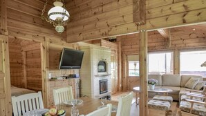 A cozy cabin interior with a dining area, a fireplace, a television, and a seating area with cushions. - Kannelpirtti 1 by Interhome (Liperi)