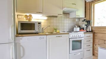 Une cuisine de taille réduite, dotée d’appareils électroménagers blancs, notamment un four à micro-ondes, un lave-vaisselle et un four traditionnel.