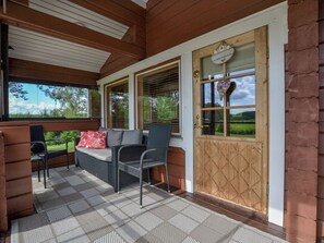 Eine überdachte Veranda mit Sitzgelegenheit, darunter eine Couch und Stühle, sowie eine Holztür mit Fenster.