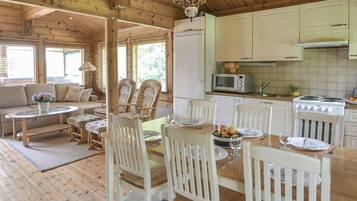 A wooden cabin interior with a dining area, kitchen, and a living room with a sofa and chairs.