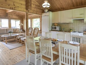 Een houten chalet van binnen met een eethoek, keuken en woonkamer met een bank en stoelen.