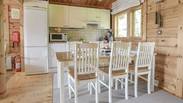 Interior em madeira com mesa e cadeiras de jantar, cozinha equipada e janela com cortinas.