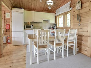 Interior em madeira com mesa e cadeiras de jantar, cozinha equipada e janela com cortinas.