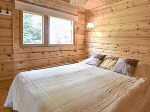 Ein Zimmer in einer Holzhütte mit einem Bett, einem Fenster und einer Wandlampe.