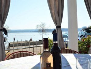 Une table avec une bouteille de vin et un verre, donnant sur une étendue d’eau où l’on aperçoit des personnes au loin.