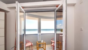Ein Zimmer mit einer Glasschiebetür, die auf einen Balkon mit Meerblick führt. Auf dem Balkon befinden sich zwei Stühle und ein kleiner Tisch.
