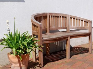 A wooden bench with a curved backrest and a slatted seat, positioned against a white wall.