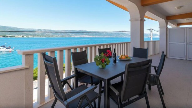 Un balcon avec une table et des chaises, donnant sur une étendue d’eau et sur une terre lointaine.