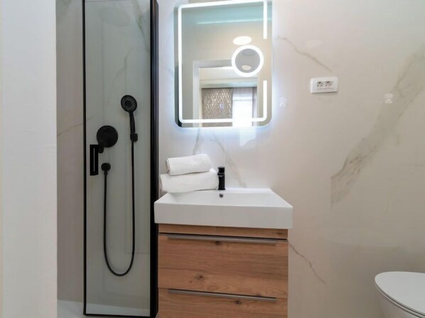 Een moderne badkamer met een douchecabine van glas, een witte wastafel met spiegel en houten kastjes.