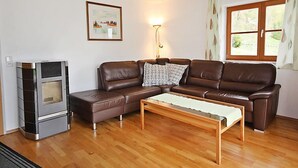 Een woonkamer met een bruine leren bank, een houten salontafel, een open haard en een raam met gordijnen.