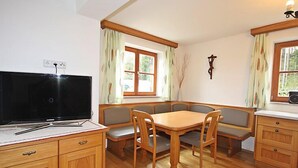 Een gezellige kamer met een houten eettafel, bankjes, een televisie en een kast.