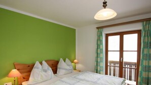 Een slaapkamer met een houten bed, groene wanden, een raam met uitzicht en een plafondlamp.