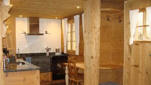 Een compacte keuken met houten wanden, een inbouwfornuis en een eethoek met een houten tafel en stoelen.