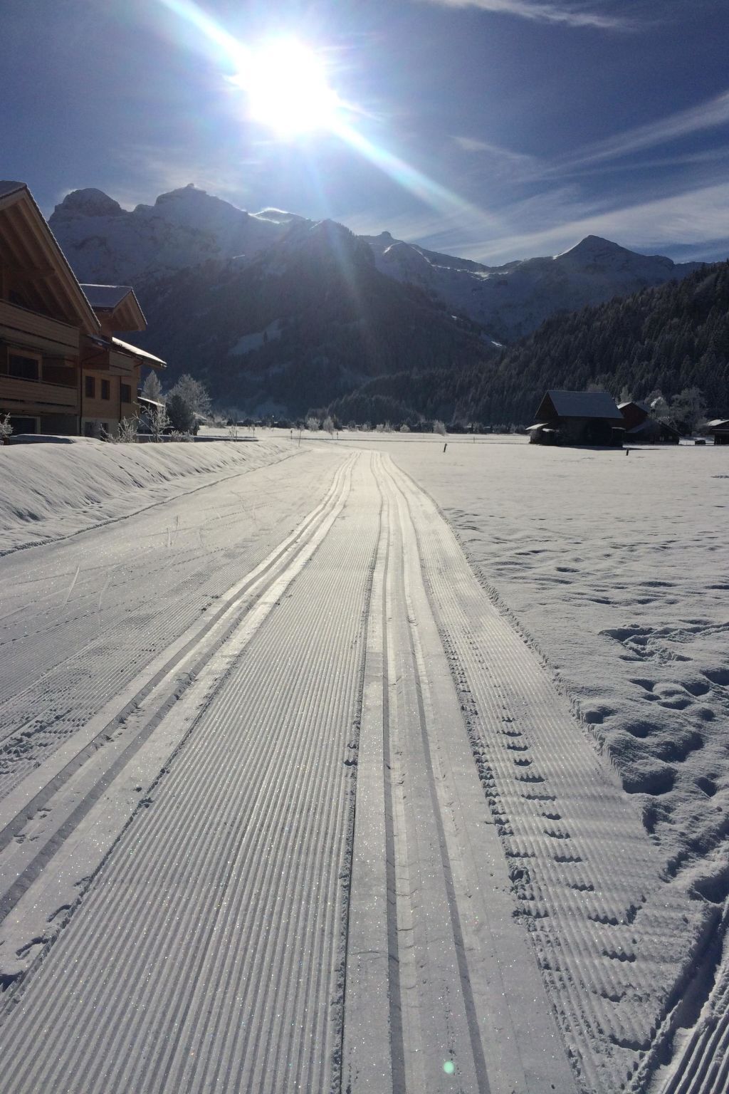 A snow-covered road with tire tracks leading to a building with a sloped roof.