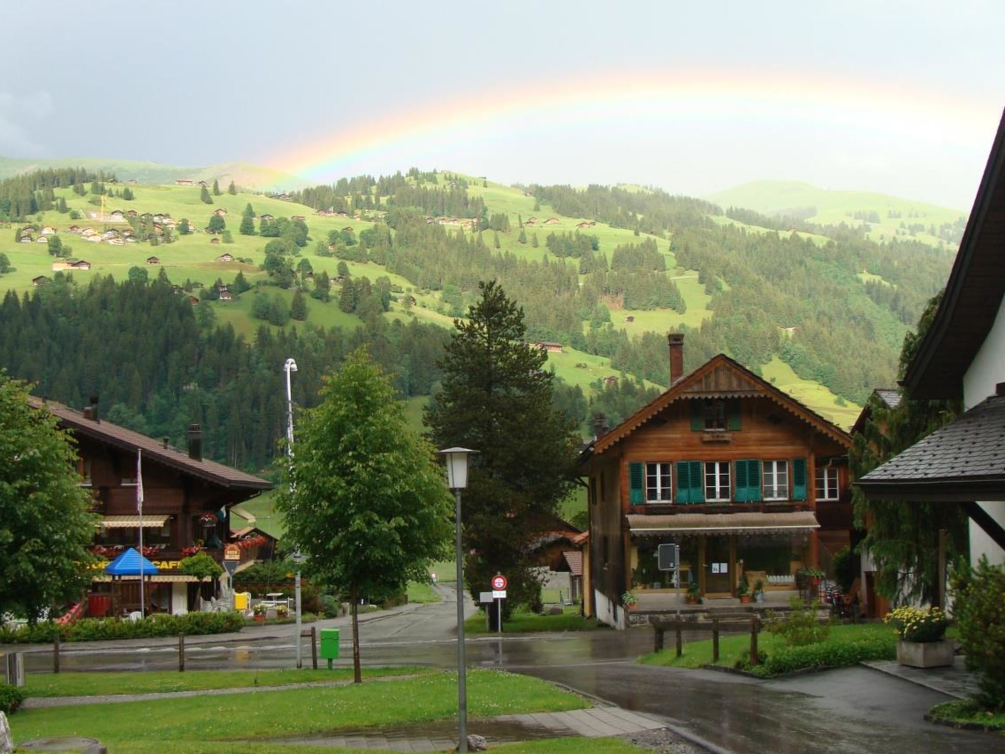 Un village rural avec des maisons traditionnelles en bois, un café et une vue sur des collines verdoyantes.