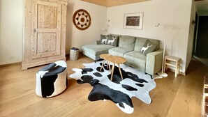 A cozy living room with a wooden ceiling, a sofa set, a round coffee table, a cowhide rug, and a cabinet.