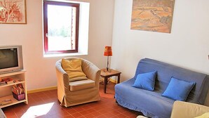 Ein Wohnzimmer mit einer Couch, einem Sessel, einem Fernseher und einem kleinen Tisch mit einer Lampe.