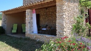 Ein Steingebäude mit überdachter Terrasse, zwei grünen Stühlen und einem Tisch.