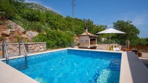 A rectangular pool with clear blue water, surrounded by a stone wall and metal ladder. - Apartment Sanja by Interhome (Karlobag)