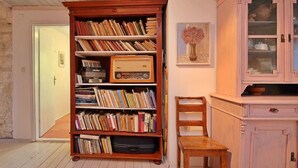 Habitació amb una estant de fusta plena de llibres i un aparell de ràdio antic, una cadira de fusta i un armari rosa amb portes de vidre.