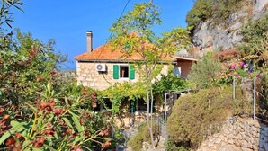 Una casa de pedra amb teulada ceràmica, envoltada de vegetació i una paret de pedra.
