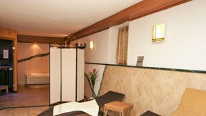 Une salle de spa équipée d’une table de massage, d’un petit tabouret en bois et d’un espace séparé avec une baignoire.