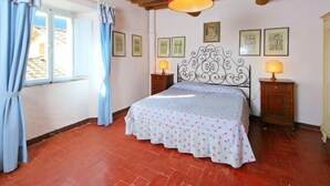 Une chambre à coucher avec un lit, des poutres en bois au plafond, une fenêtre avec des rideaux et des tableaux encadrés accrochés au mur.