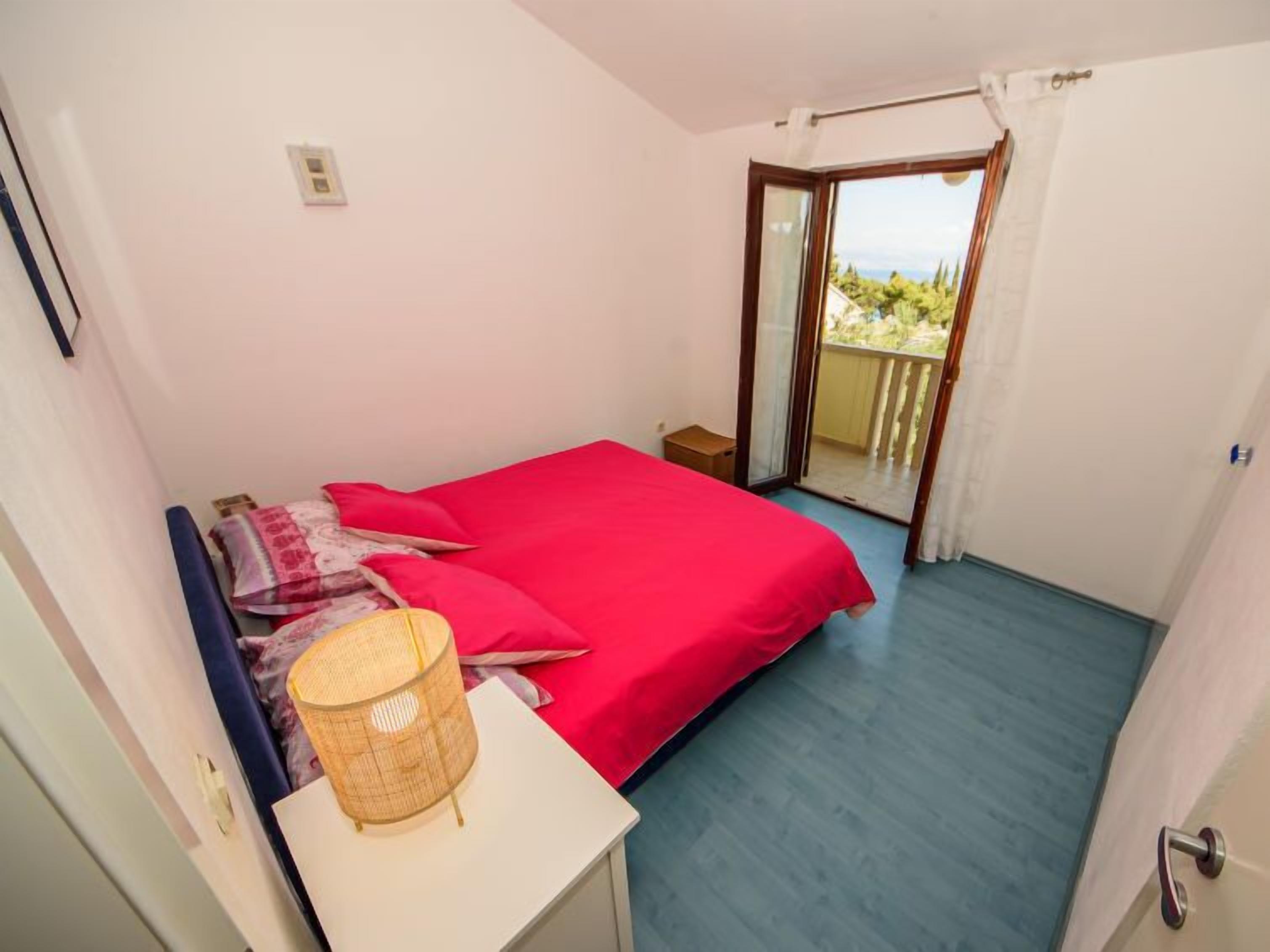 A bedroom with a bed, a small bedside table, a lamp, and a sliding glass door leading to a balcony.