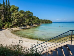 Une plage à l’eau claire, avec un rivage sablonneux et un escalier qui descend vers la plage.