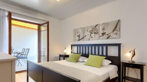 A bedroom with a large bed, two bedside tables, a desk, and a chair. There are three wall-mounted artworks above the bed.