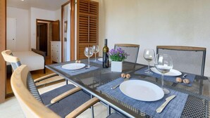 A dining area with a table set for two, a chair, and a small table with a bottle and flowers.