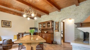A spacious dining area with a large wooden table, a stone fireplace, and a rustic stone wall.