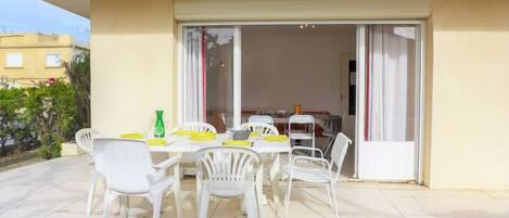 A patio with a table and chairs, a sliding glass door leading to an interior space, and a view of the surrounding area.